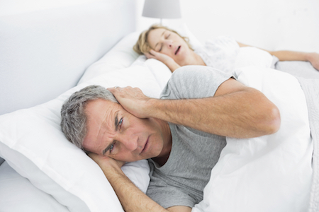 Man covering ears to down out wife's snoring which is a symptom of sleep apnea. 